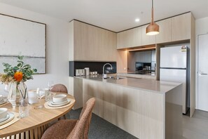 A modern kitchen with a central island, stainless steel appliances, and a dining area with a round table and chairs. - Premium Urban Stay – Rooftop Pool, City Vista (Newstead)