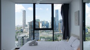 Una habitació d'hotel amb un llit gran, un ventilador de sostre i una vista a la ciutat a través de finestres del terra al sostre.