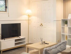 A living room with a TV, a lamp, a coffee table, and a bookshelf.
