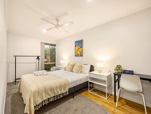 A bedroom with a bed, desk, chair, and a ceiling fan.