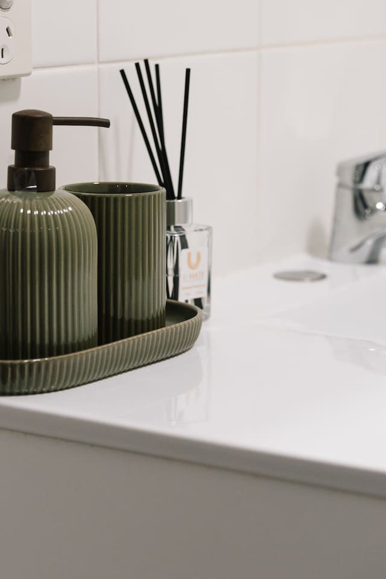 Un lavabo de salle de bain avec un distributeur de savon vert et un récipient en verre contenant des bâtonnets noirs.