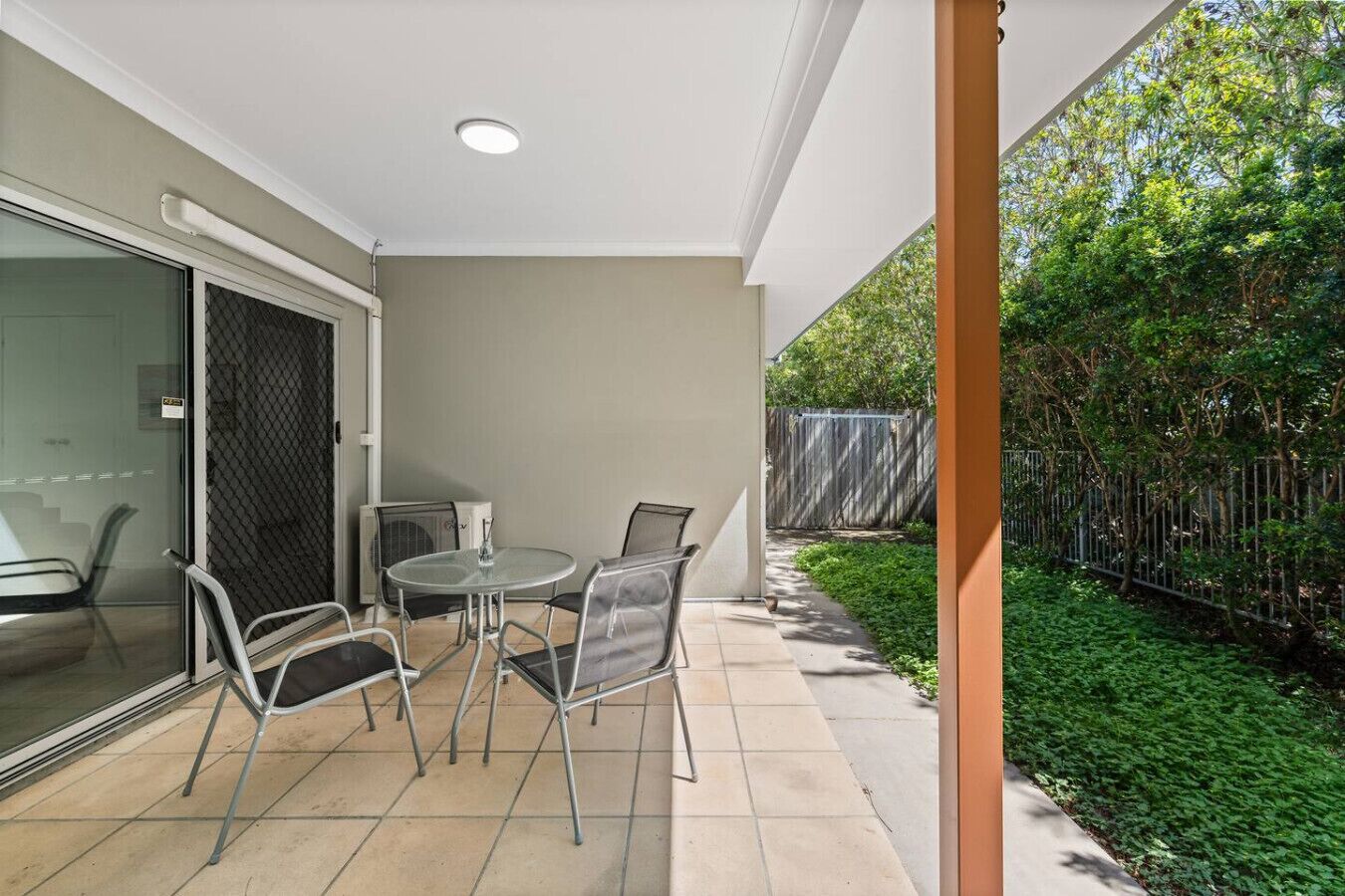 A patio with a table and chairs, a glass door, and a view of a garden with a fence.
