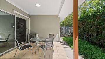 A patio with a table and chairs, a glass door, and a view of a garden with a fence.