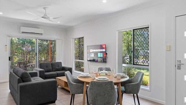 Una sala de estar moderna con un conjunto de sofá, una mesa de comedor, sillas y un televisor montado en la pared.