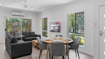 A modern living room with a sofa set, dining table, chairs, and a TV mounted on the wall.