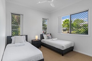 A bedroom with two beds, a nightstand, a ceiling fan, and large windows with a view of greenery. - Comfort Nest|2BR Quiet Comfort Retreat for Relax (Mount Warren Park)