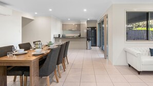 A modern kitchen with a dining area, a white sofa, and a large window. - 4BR Family Retreat | AC Throughout & Spacious (Park Ridge)