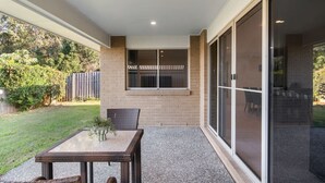 A patio area with a table and chairs, a brick wall, a window, and a sliding glass door. - 4BR Family Retreat | AC Throughout & Spacious (Park Ridge)