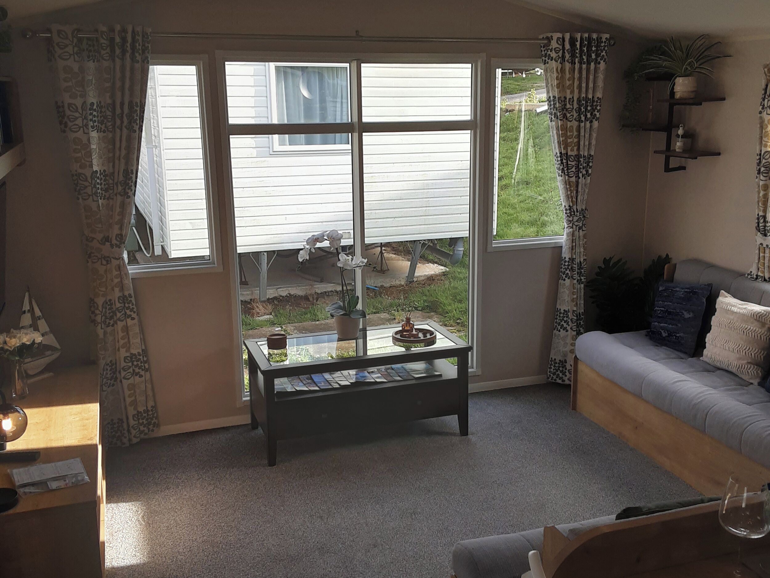A living room with a glass coffee table, a sofa, and a window with curtains.