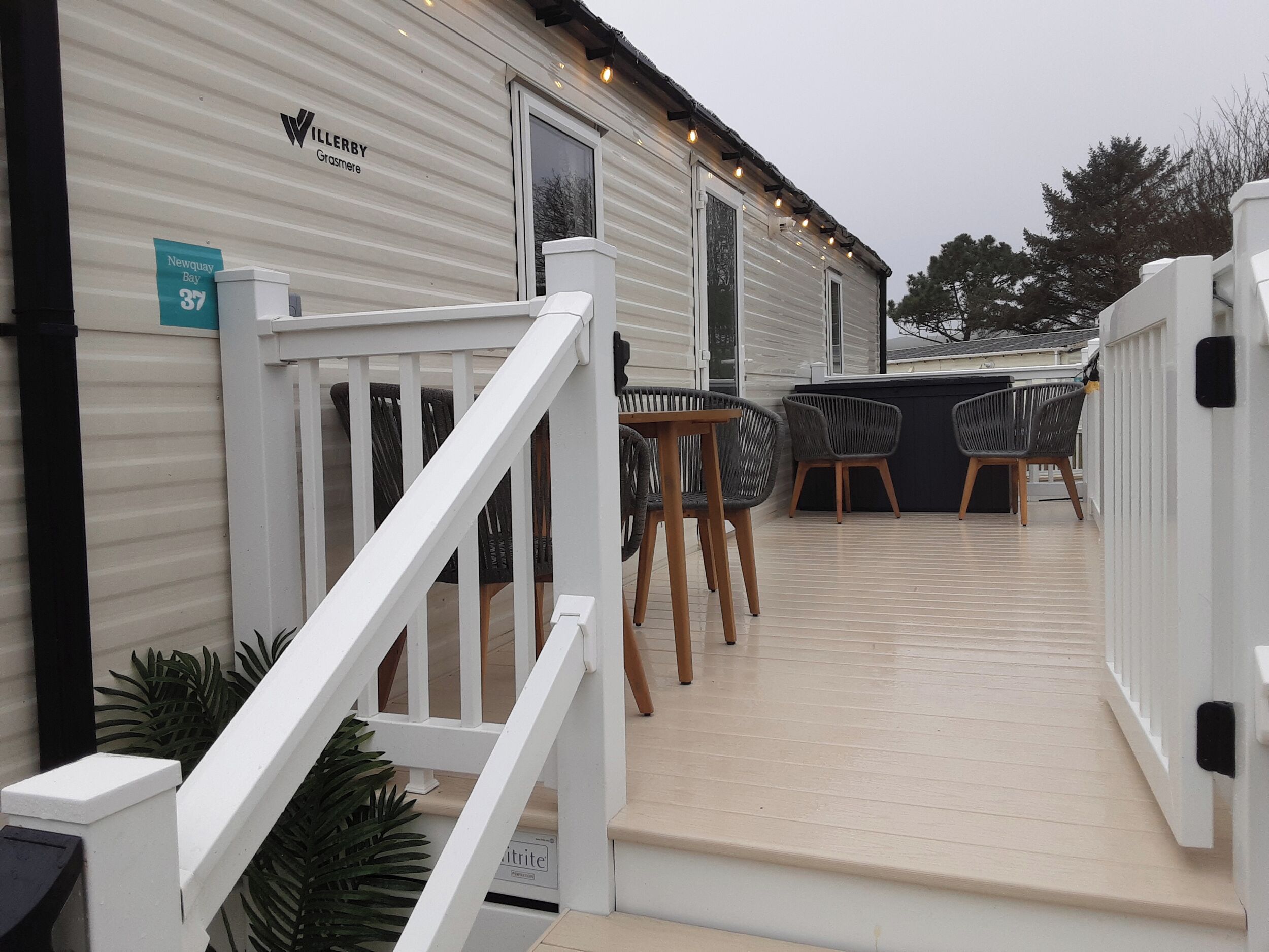 Uma casa móvel com fachada branca, um deck com área de estar externa e uma escadaria que leva à entrada.