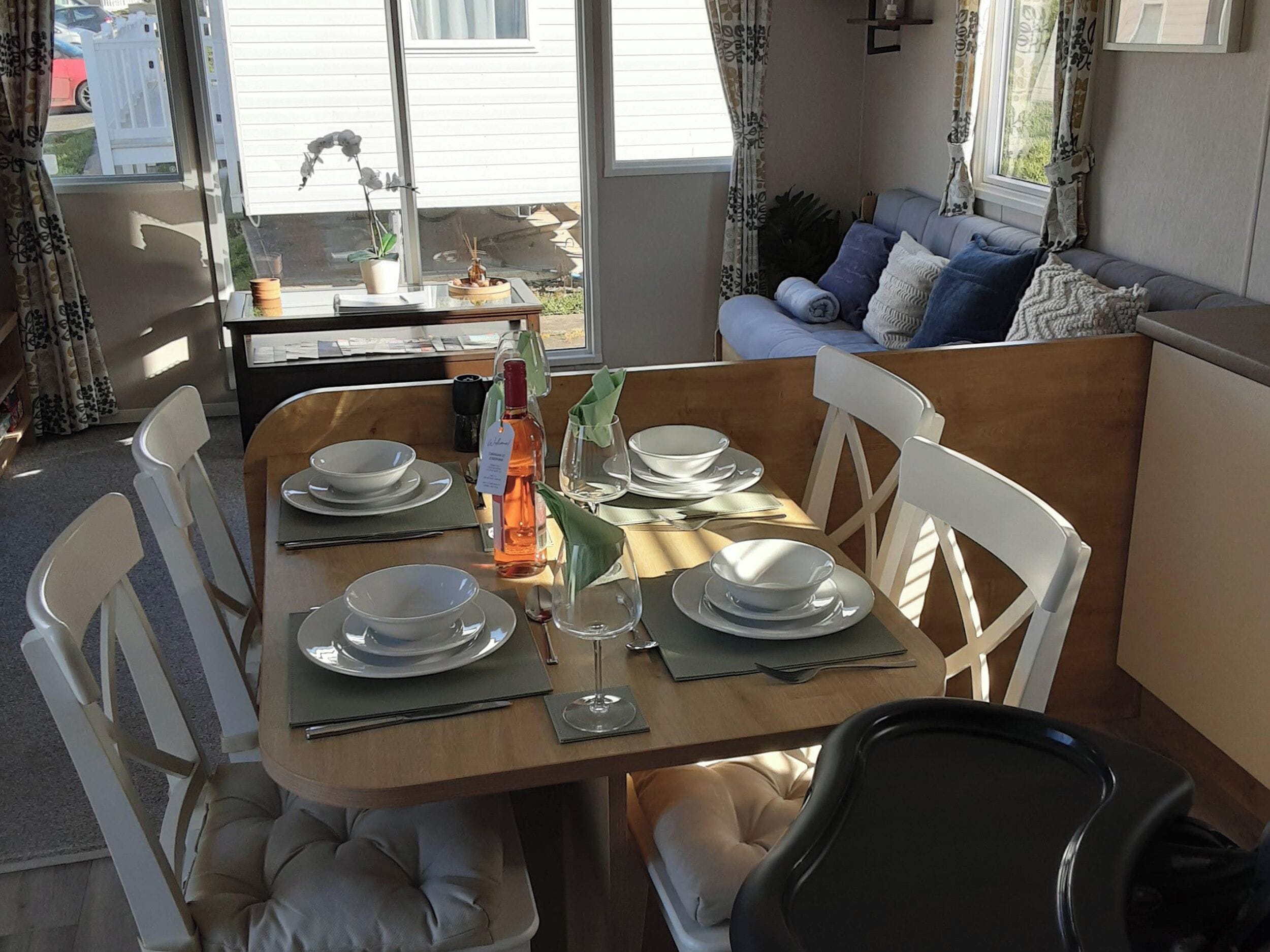 A dining table set for four with white chairs, a bottle of wine, and a small potted plant.