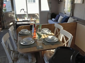 A dining table set for four with white chairs, a bottle of wine, and a small potted plant. - Josephine Nb37 (Newquay)