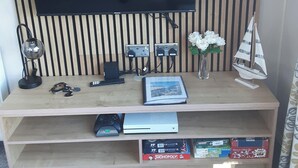 A wooden desk with a flat-screen TV, a lamp, a remote, a vase with flowers, and a model sailboat. - Josephine Nb37 (Newquay)