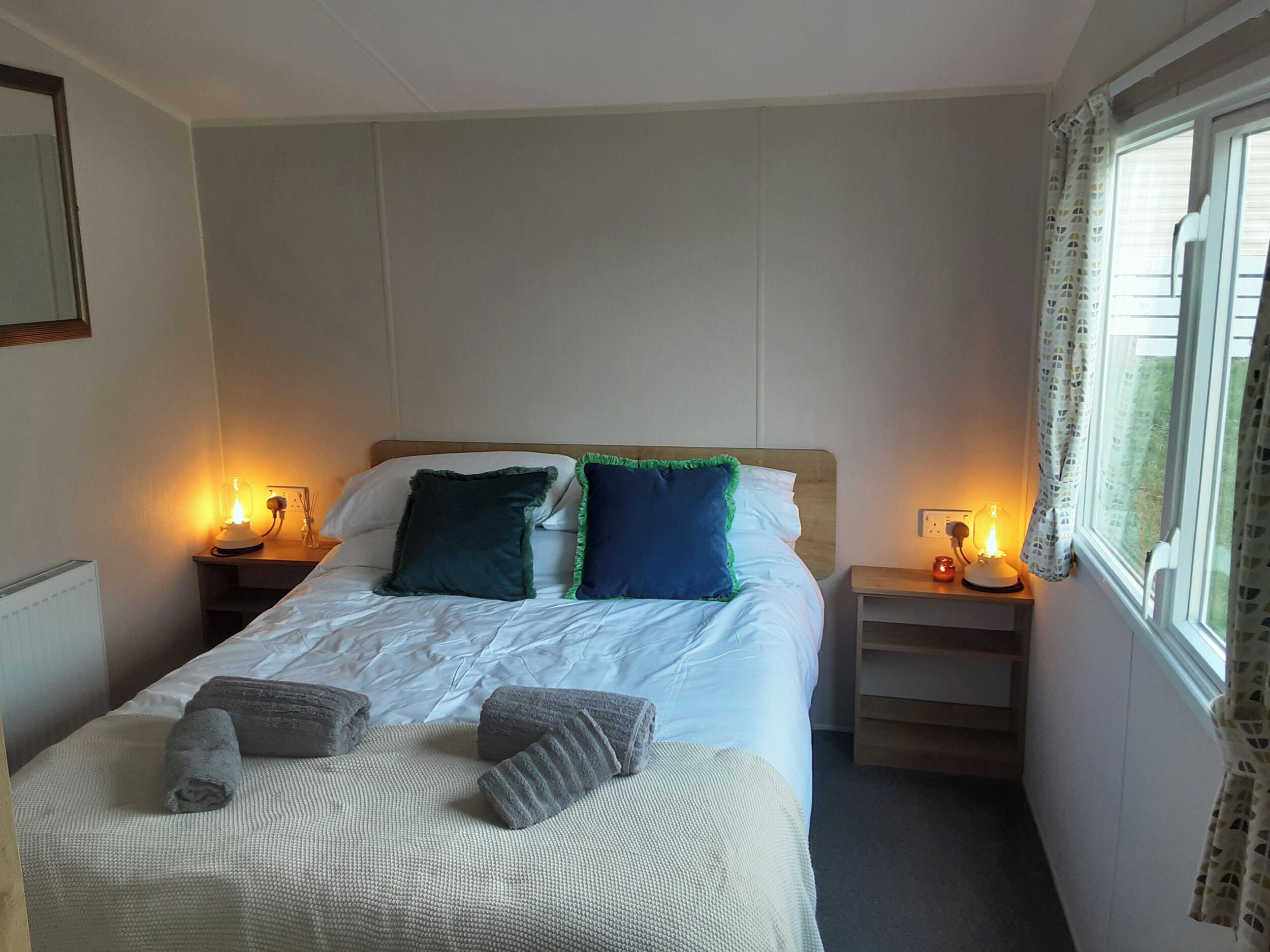 A hotel room with a bed, two bedside lamps, a window with curtains, and a radiator.