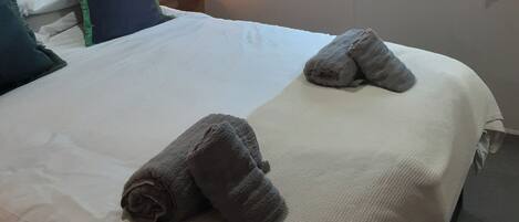 A neatly made bed with two rolled towels, a bedside lamp, and a window with a view.