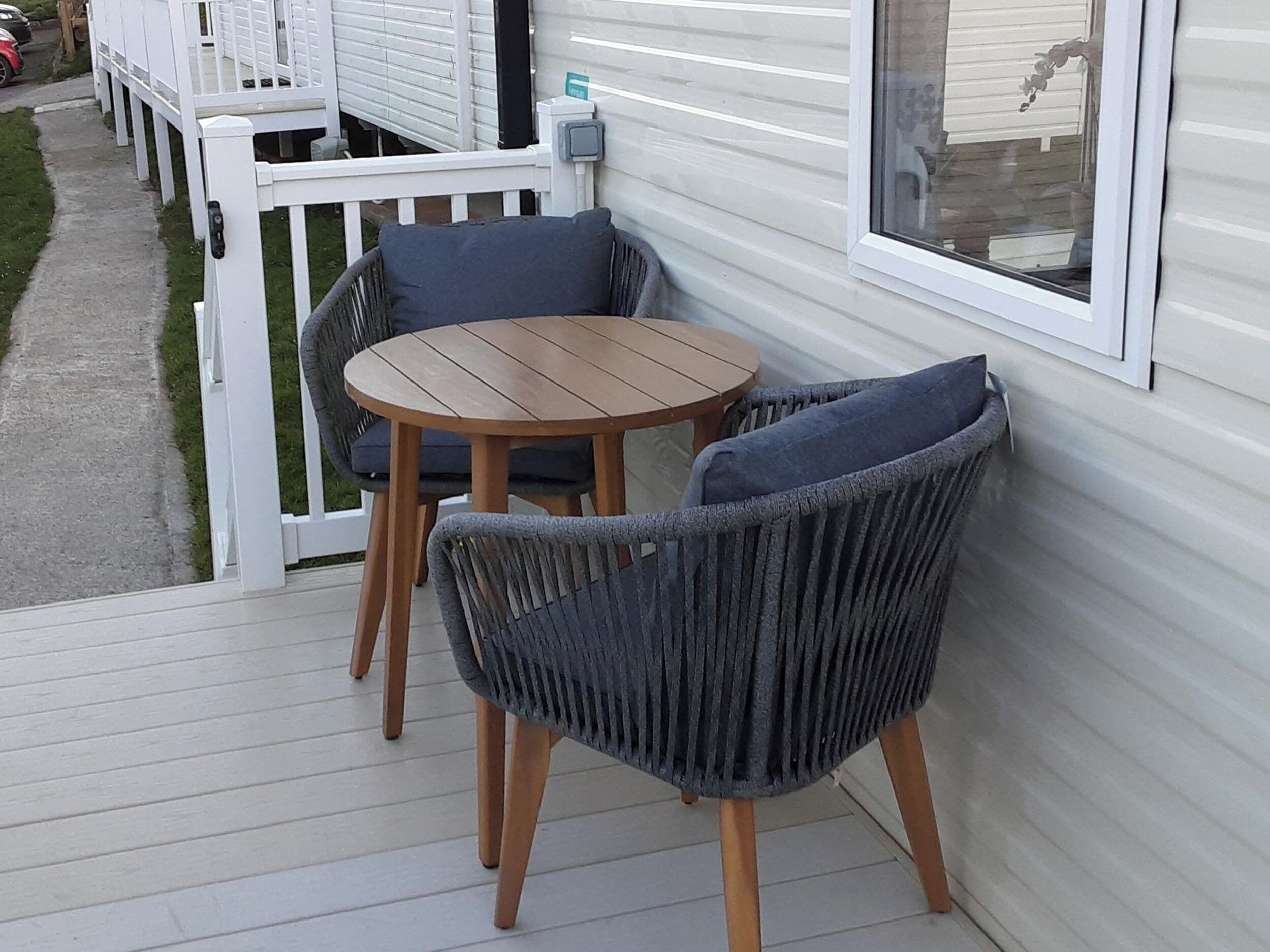 A deck with two chairs and a table, a white railing, and a window.
