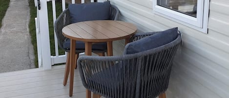 A deck with two chairs and a table, a white railing, and a window.