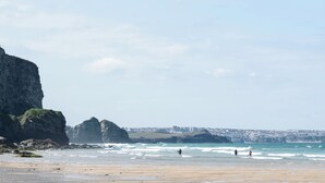 A coastal beach with rocky cliffs, waves, and surfers. - Josephine Nb37 (Newquay)