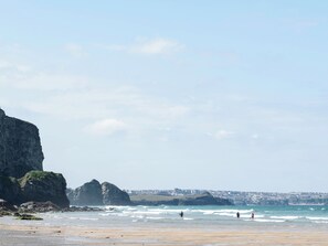 A coastal beach with rocky cliffs, waves, and surfers. - Josephine Nb37 (Newquay)