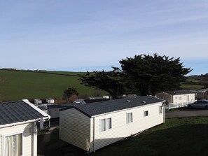 A row of mobile homes with a grassy field and a large tree in the background. - Josephine Nb37 (Newquay)