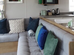 A modern living room with a grey sofa, a wooden coffee table, and a kitchen area with a kettle and jars. - Josephine Nb37 (Newquay)