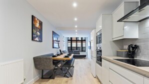 Uma cozinha moderna com armários brancos, uma sala de jantar com mesa e cadeiras, e uma janela grande que proporciona iluminação natural.