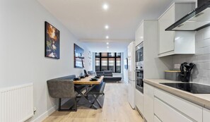 Eine moderne Küche mit weißen Schränken, ein Essbereich mit Tisch und Stühlen sowie ein großes Fenster für natürliches Licht.