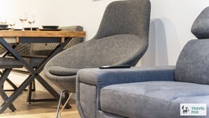 Um interior moderno com um sofá estofado cinza, uma mesa de madeira com copos e tigelas, e uma cadeira preta com estrutura de metal.
