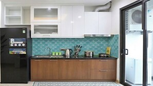 A kitchen with a black refrigerator, wooden cabinets, a tiled backsplash, and a sliding glass door leading to a balcony. - Boho Apartment Tay Ho (Hanoi)