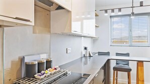 A modern kitchen with a built-in stove, coffee machine, and a bar area with stools.