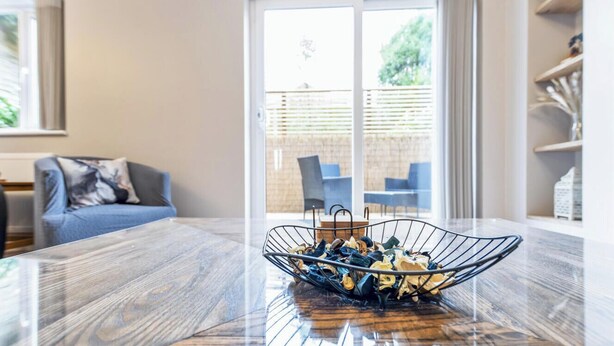 A dining table with a metal bowl in the center, a sofa, and a sliding glass door leading to an outdoor area.