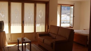 A living room with a sofa, a small table, a TV, and a sliding door with curtains.