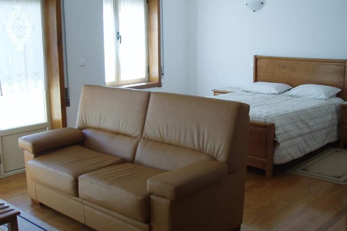 A room with a sofa, a bed, a window, and a wall-mounted light fixture.
