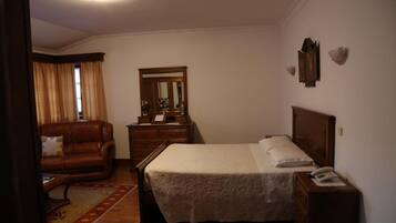 A bedroom with a bed, a dresser, a nightstand, a mirror, a window with curtains, and a leather armchair.