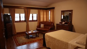 A hotel room with a bed, a leather armchair, a wooden dresser, a television, and a desk with a telephone.