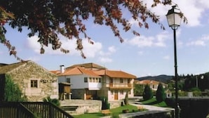 A stone house with a red roof, a wooden staircase, and a small pond.