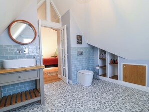 A bathroom with a sink, toilet, and shower area, featuring blue and white patterned tiles. - The Old Dairy (Honiton)