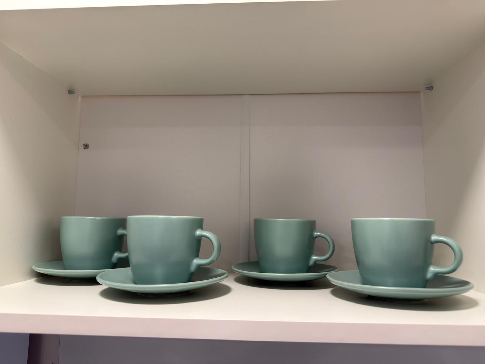 Une étagère avec quatre tasses et soucoupes de couleur turquoise.