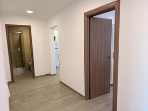 En hall med en dörr av trä, en duschkabin med glasväggar och en vit toalett som syns i bakgrunden.