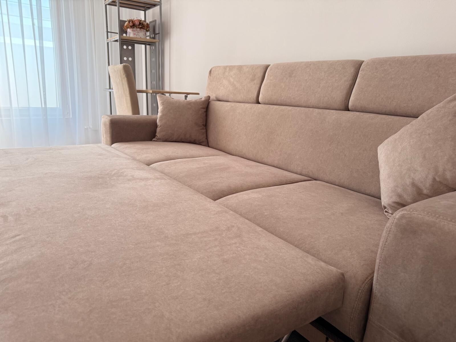 Un sofá seccional color beige en una sala de estar moderna, con un estante metálico contra la pared.