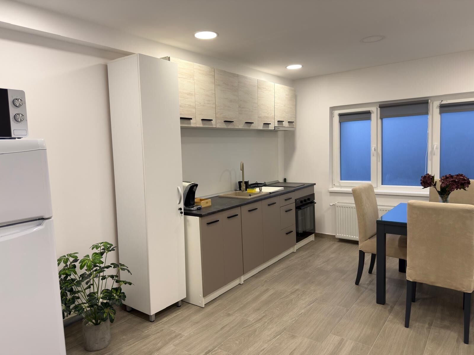 Una cuina moderna amb forn integrat, zona de dinar amb taula i cadira, i finestra amb vistes.