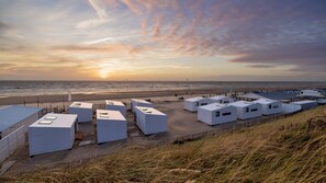 Un hôtel en bord de mer, doté de plusieurs bungalows blancs, offrant une vue sur la plage et un magnifique coucher de soleil en arrière-plan.