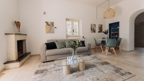 Un salon comprenant une table basse en verre, un canapé, une cheminée et un coin repas avec des chaises.