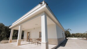 Un espace extérieur abrité, équipé d’un banc, d’une table et d’une porte donnant accès à l’intérieur.