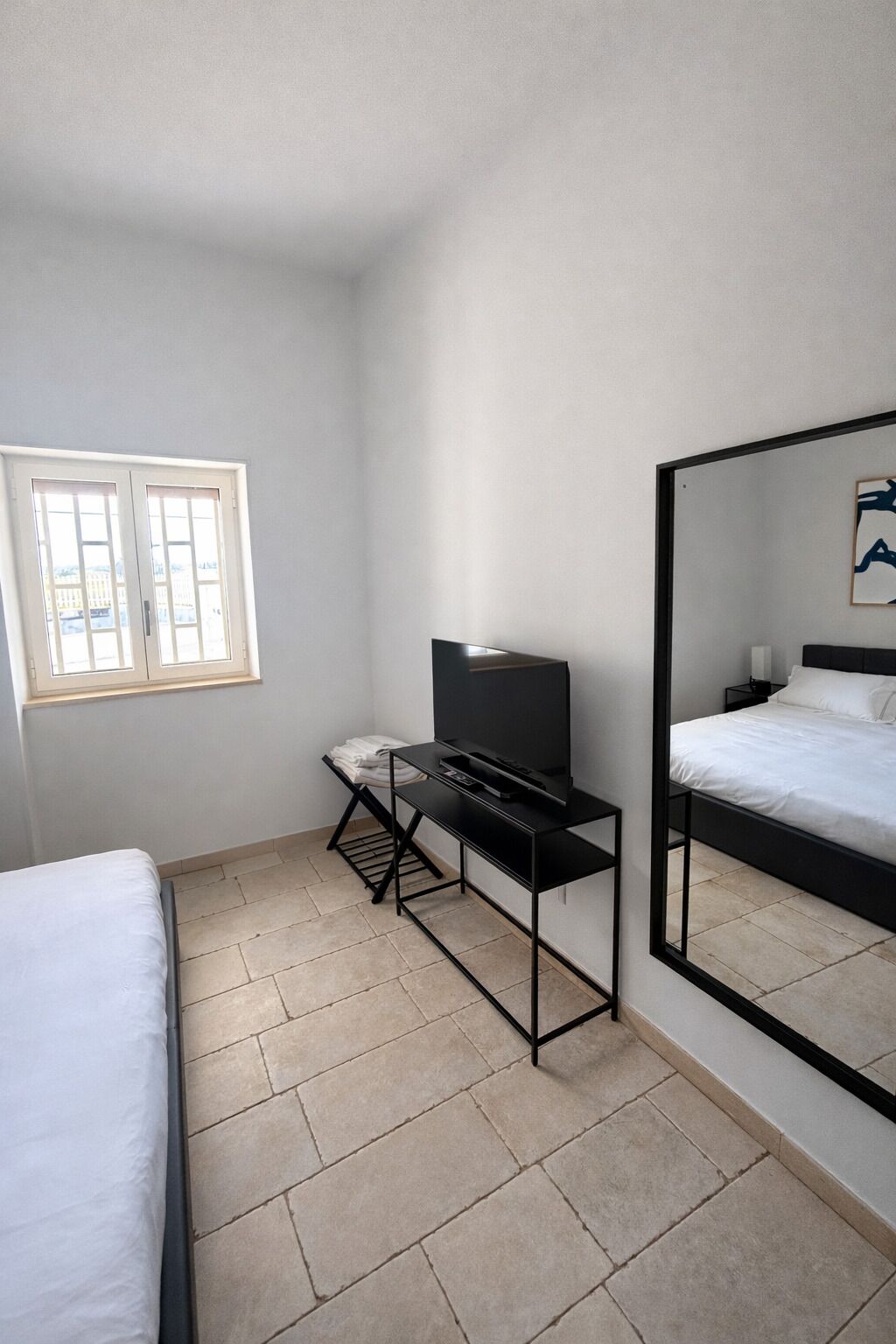 Une chambre à coucher avec un lit, un téléviseur posé sur un meuble, une fenêtre et un miroir.