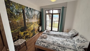 Ein Schlafzimmer mit Waldgemälde, zwei Betten mit floraler Bettwäsche, ein Holzstuhl und ein Balkon mit Blick.