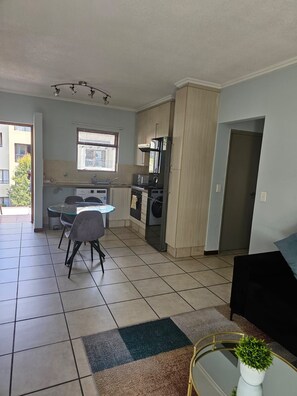 A compact kitchen with a dining area, a washing machine, and a refrigerator. - Exquisite one-bedroom Apartment In Fourways (Sandton)