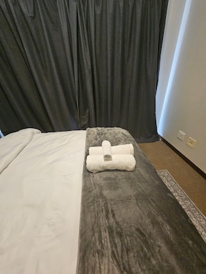 A hotel room with a bed, a grey headboard, a white towel, and a small rug. - Exquisite one-bedroom Apartment In Fourways (Sandton)