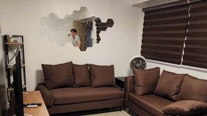 Un salon avec un canapé marron, une table d’appoint en bois, un téléviseur et un élément décoratif mural.