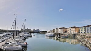 A marina with boats docked, a stone embankment, and buildings with balconies. - Appartement avec terrasse ensoleillée sur le port Olona (Les Sables-d'Olonne)